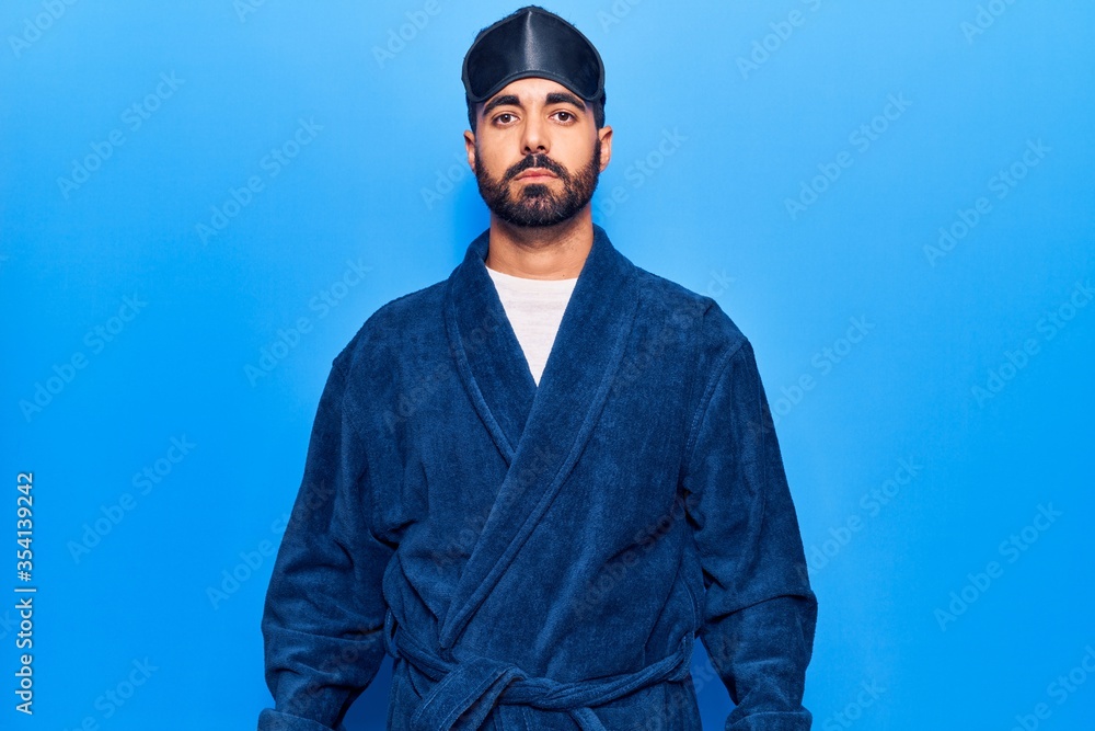 Poster Young hispanic man wearing sleep mask and robe with serious expression on face. simple and natural looking at the camera.