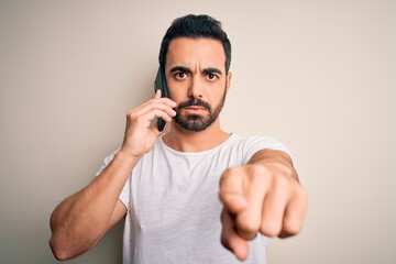 Young handsome man with beard having conversation talking on the smartphone pointing with finger to the camera and to you, hand sign, positive and confident gesture from the front