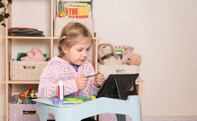Little girl with scissors and glue. Portrait of a little cute girl cutting a paper with tablet computer. Distance learning online education.
