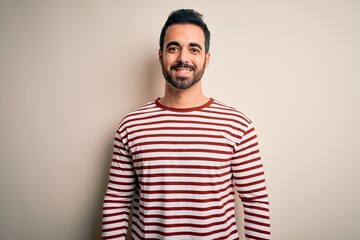 Young handsome man with beard wearing casual striped t-shirt standing over white background with a happy and cool smile on face. Lucky person.