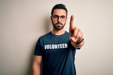Handsome man with beard wearing t-shirt with volunteer message over white background Pointing with...