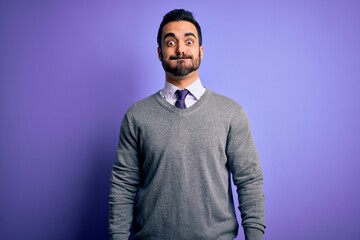 Handsome businessman with beard wearing casual tie standing over purple background puffing cheeks with funny face. Mouth inflated with air, crazy expression.
