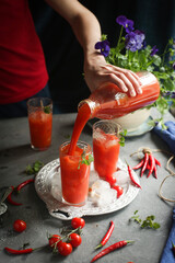 On the table are glasses with tomato juice, a hand pours juice.