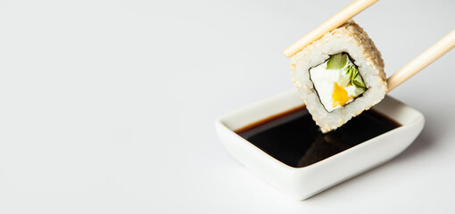 Sushi roll in sesame seeds is held with chopsticks and dipped in soy sauce soaked in soy sauce
