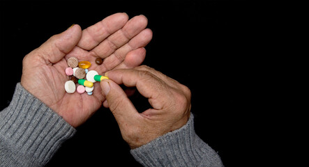 An elderly man holds a lot of colored pills in old hands. Painful old age. Health care of older people