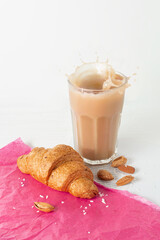French splashing coffee with croissant on the pink paper and newspaper. Cozy breakfast.