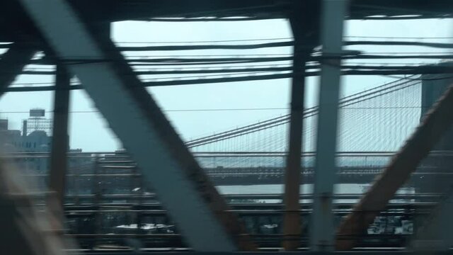 Looking out the window of a New York City subway train in motion (Brooklyn to Manhattan) going over the Manhattan Bridge with the Brooklyn Bridge in the background. Cinematic, hand-held POV shot.