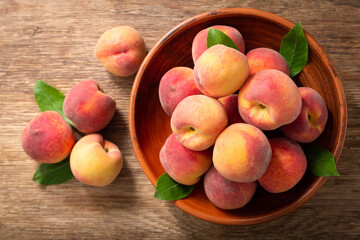 fresh ripe peaches with leaves in a bowl, top view