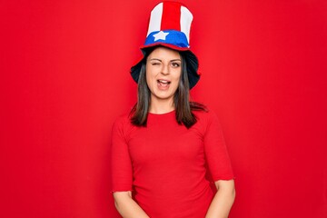 Young beautiful brunette woman wearing united states hat celebrating independence day winking...