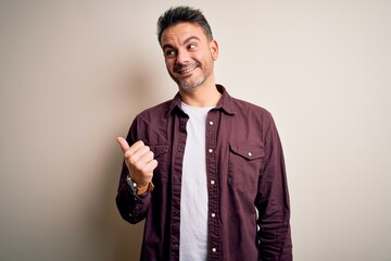 Young handsome man wearing casual shirt standing over isolated white background smiling with happy face looking and pointing to the side with thumb up.