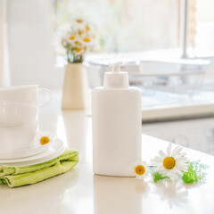 Fototapeta na wymiar Eco friendly non-toxic cleaning dish soap with natural ingredients, chamomile flowers, clean white cups and plates on white kitchen table. Skincare for housekeeping. Bio organic cleaning supplies.