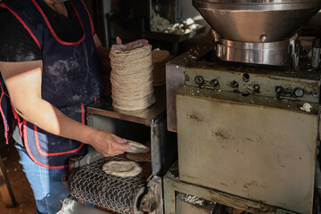 La mujer está acomodando las tortillas calientes que están saliendo de la maquina.