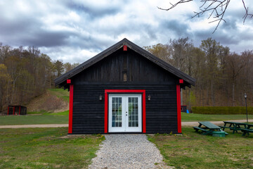 beautiful small historic building  barn in red and black with a white door in spring in Canada, Quebec