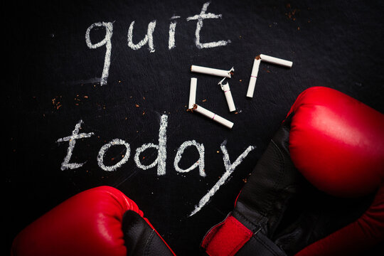 Stop smoking concept. Broken cigarettes and boxing gloves with the words -Quit today on a black background.