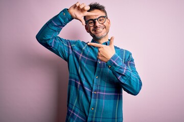 Young handsome man wearing casual shirt and glasses standing over isolated pink background smiling making frame with hands and fingers with happy face. Creativity and photography concept.