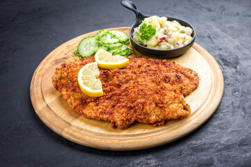 Traditionelles frittiertes Wiener Schnitzel mit Kartoffel und Gurken Salat angeboten als closeup auf einem rustikalen Holz Board