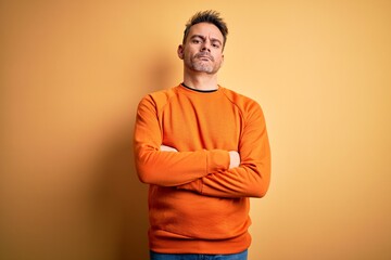 Young handsome man wearing orange casual sweater standing over isolated yellow background skeptic...