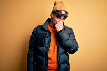 Young handsome skier man skiing wearing snow sportswear using ski goggles smelling something stinky...