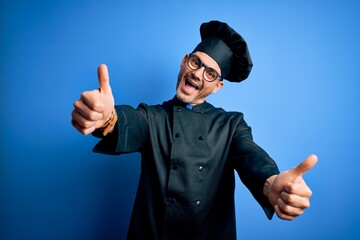 Young handsome chef man wearing cooker uniform and hat over isolated blue background approving...