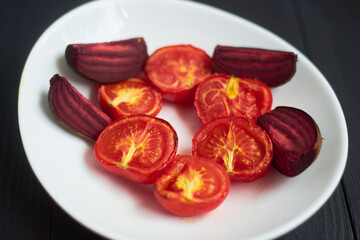 Grilled baked tomatoes and beet in the oven on a white plate.