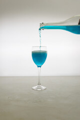 Blue glitter drink pours into a glass from a bottle on a light background. Sparkling blue wine.