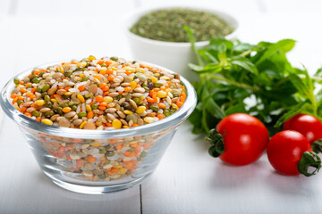 Colorful various beans or lentils and whole grains seeds or cereal in bowl with fresh vegetables on wooden background.