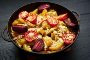 Cooked potato, baked with tomatoes, bacon and cheese in a pan.