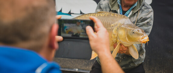 Unknown man photographing a big fish caught in the lake as a souvenir.