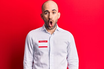 Young handsome bald man wearing hello my name is sticker scared and amazed with open mouth for surprise, disbelief face