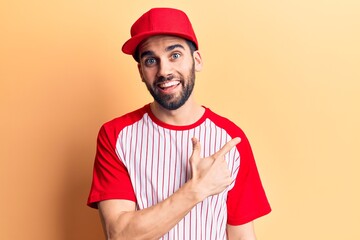 Young handsome man with beard wearing baseball cap and t-shirt smiling cheerful pointing with hand and finger up to the side