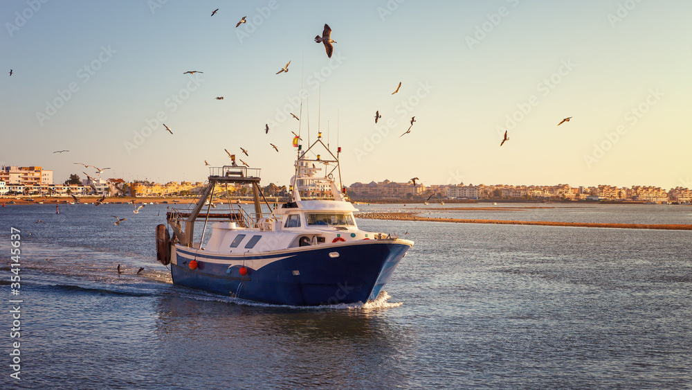 Wall mural fishing boat at sunset arriving at the port of isla cristina, after a long day at work in the waters