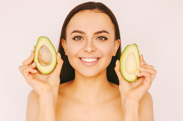 Portrait happy beautiful brunette woman hold avocado slices in hands and smile isolated on white background. Young attractive girl with healthy smooth skin have fun with avocado. Beauty treatment