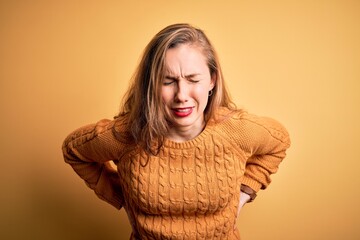 Young beautiful blonde woman wearing casual sweater standing over yellow background Suffering of backache, touching back with hand, muscular pain