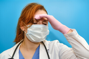 The doctor in a uniform on a blue background tiredly bowed her head, copy space. Sad nurse face...