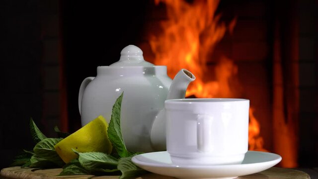 Cozy Fireplace,teapot and cup of Tea with lemon amd mint rotate in a country house.