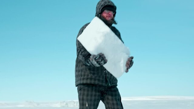bearded traveler constructs igloo with ice blocks from endless frozen sea surface under blue sky on cold sunny winter day
