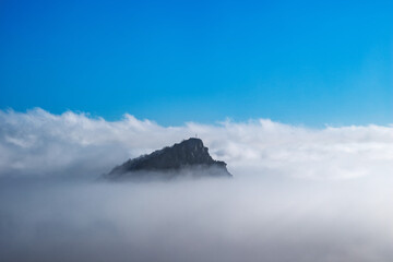 Fototapeta na wymiar The top of the mountain with a geodesic sign rises above the fog with blue sky background