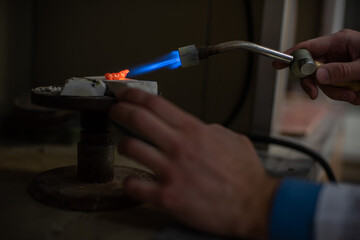 A dental technician makes partial dentures. The production of a false jaw or dental bridges using a manual gas burner. Close-up.