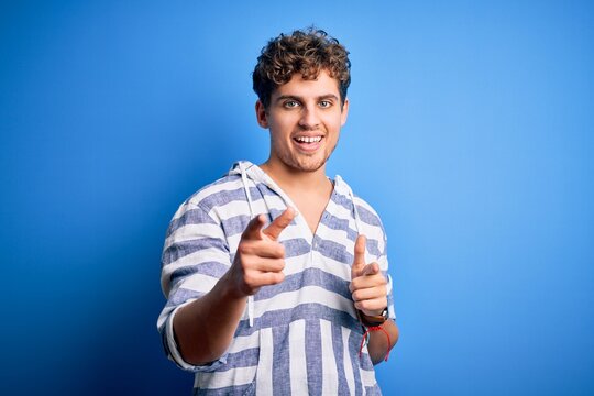 Young blond handsome man with curly hair wearing casual striped sweatshirt pointing fingers to camera with happy and funny face. Good energy and vibes.