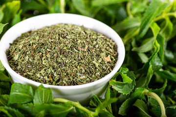 Dried peppermint in a white bowl on a bunch of fresh mint, on wooden background. Food background.