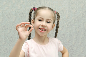 little girl smiles and holds a lost milk tooth in her hands, selective focus, pastel colors