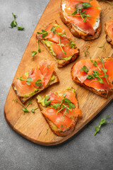 bruschetta with trout or salmon and avocado on a wooden board decorated with microgreens