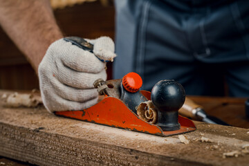 A man carpenter engaged in woodworking planes the surface of a wooden Board in his workshop with a hand plane. Concept of repair and construction