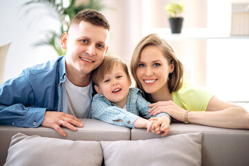 Obraz premium Family portrait. A happy family. Handsome dad, attractive mom and their little adorable smiling son are sitting on the sofa in their cozy apartment