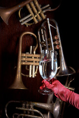 pipes of wind instruments on a wooden background in the center of a gloved hand with a ring holding a glass with a drink.
