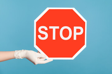 Profile side view closeup of human hand in white surgical gloves holding and showing Stop sign....