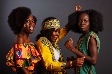 Three young beautiful African fashion models have fun and laughing in traditional dress. Women from the Congo Republic, Ivory Coast, and Zimbabwe - obrazy, fototapety, plakaty