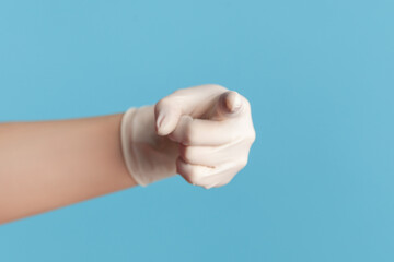 Profile side view closeup of human hand in white surgical gloves showing or pointing at camera. indoor, studio shot, isolated on blue background.