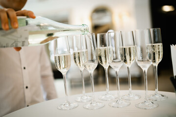 The waiter pours champagne into the glasses. Restaurant table setting. 