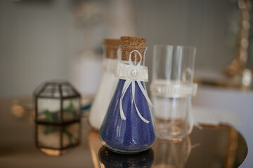 Decorative sand in glass flasks of blue and white. Wedding rings in a box in the background in blur.